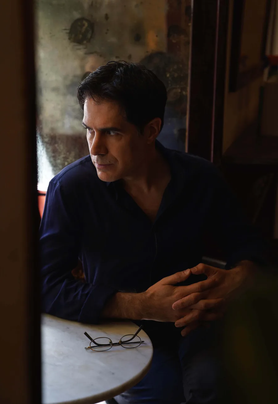 Diego Sabanés pensativo junto a una ventana, con unas gafas sobre la mesa.